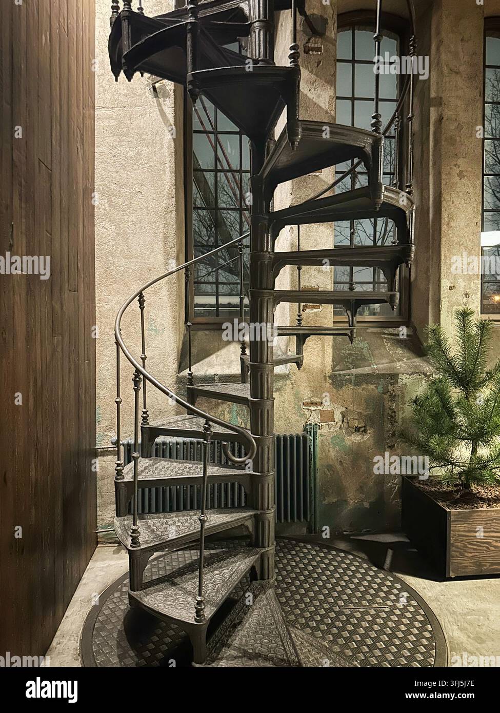 Scalinata a chiocciola industriale in un interno vintage con finestre e pino. Scalinata a chiocciola vintage in metallo nero all'interno di un edificio industriale - Immagine stock catturata con smartphone