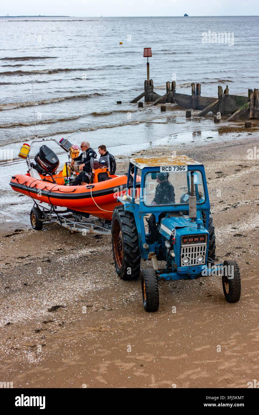 Un vecchio trattore Ford viene utilizzato per trainare un rimorchio per recuperare un motoscafo dal mare sulla spiaggia di Cleethropes nel Lincolnshire, UK Foto Stock