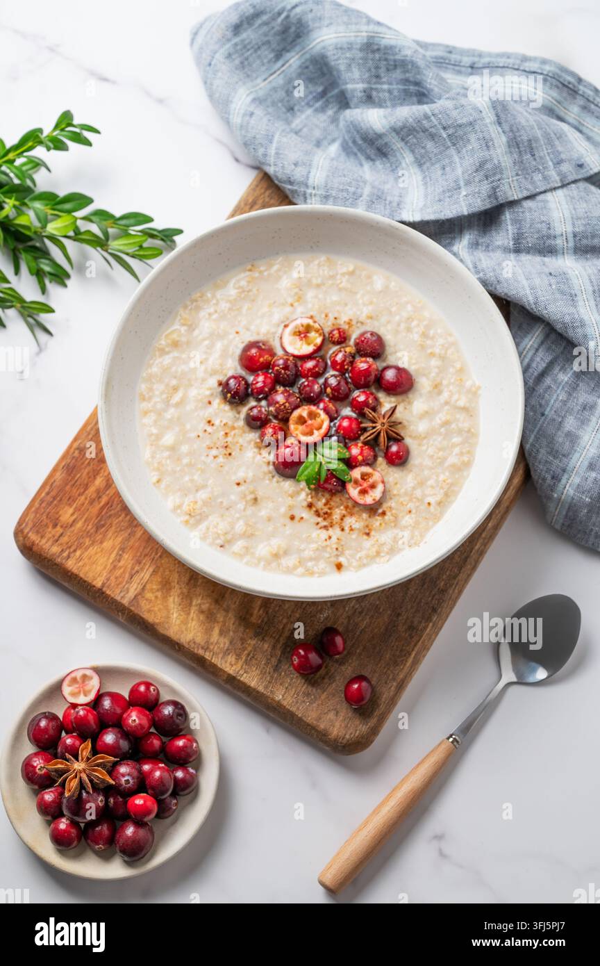 Farina d'avena con mirtillo rosso, cannella e spezie in un piatto su una tavola di legno su uno sfondo di marmo con bacche fresche, cucchiaio e tovagliolo. Concetto per una dieta sana Foto Stock