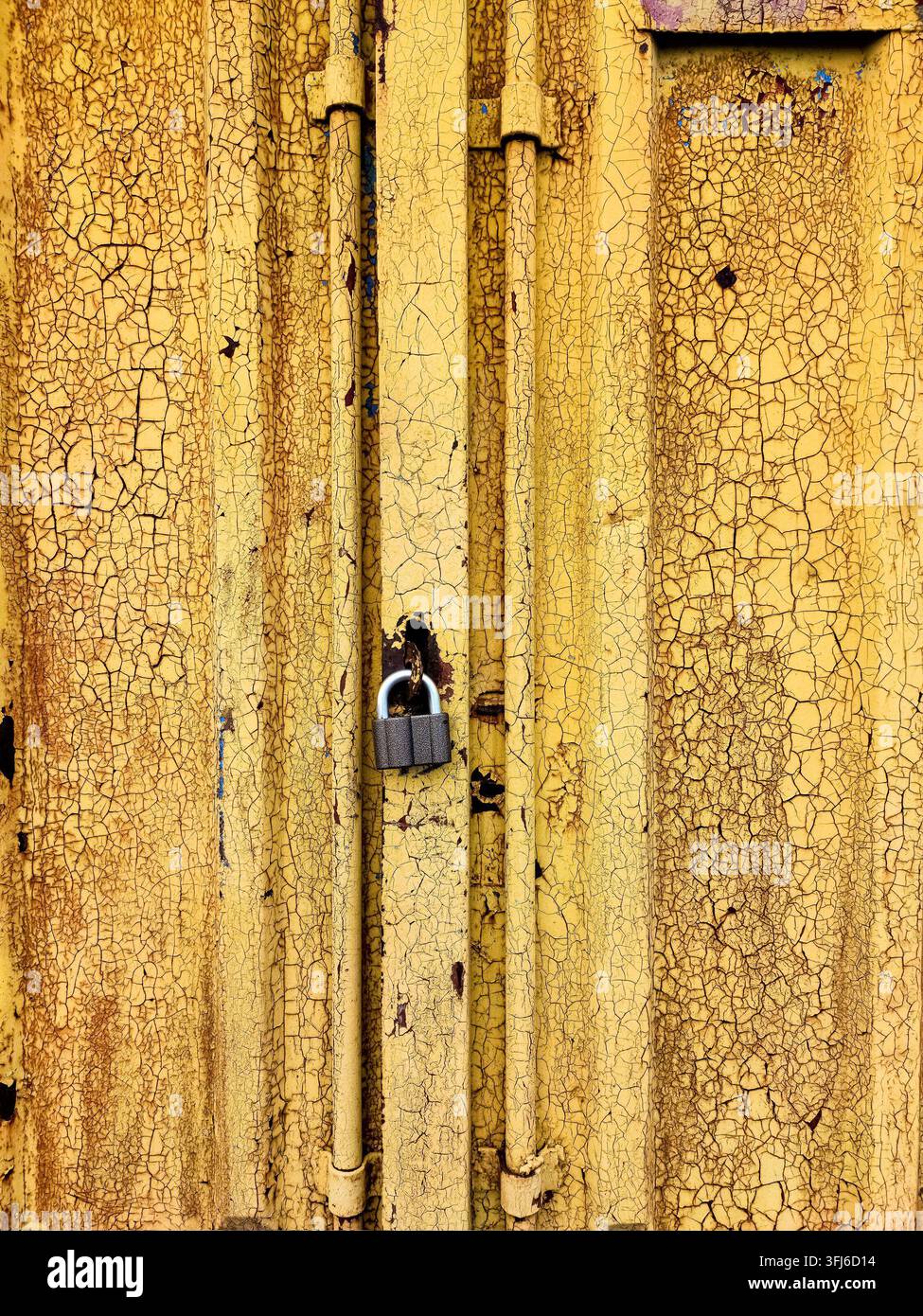 Lucchetto su una vecchia porta di metallo gialla con sfondo di vernice screpolata. Foto Stock