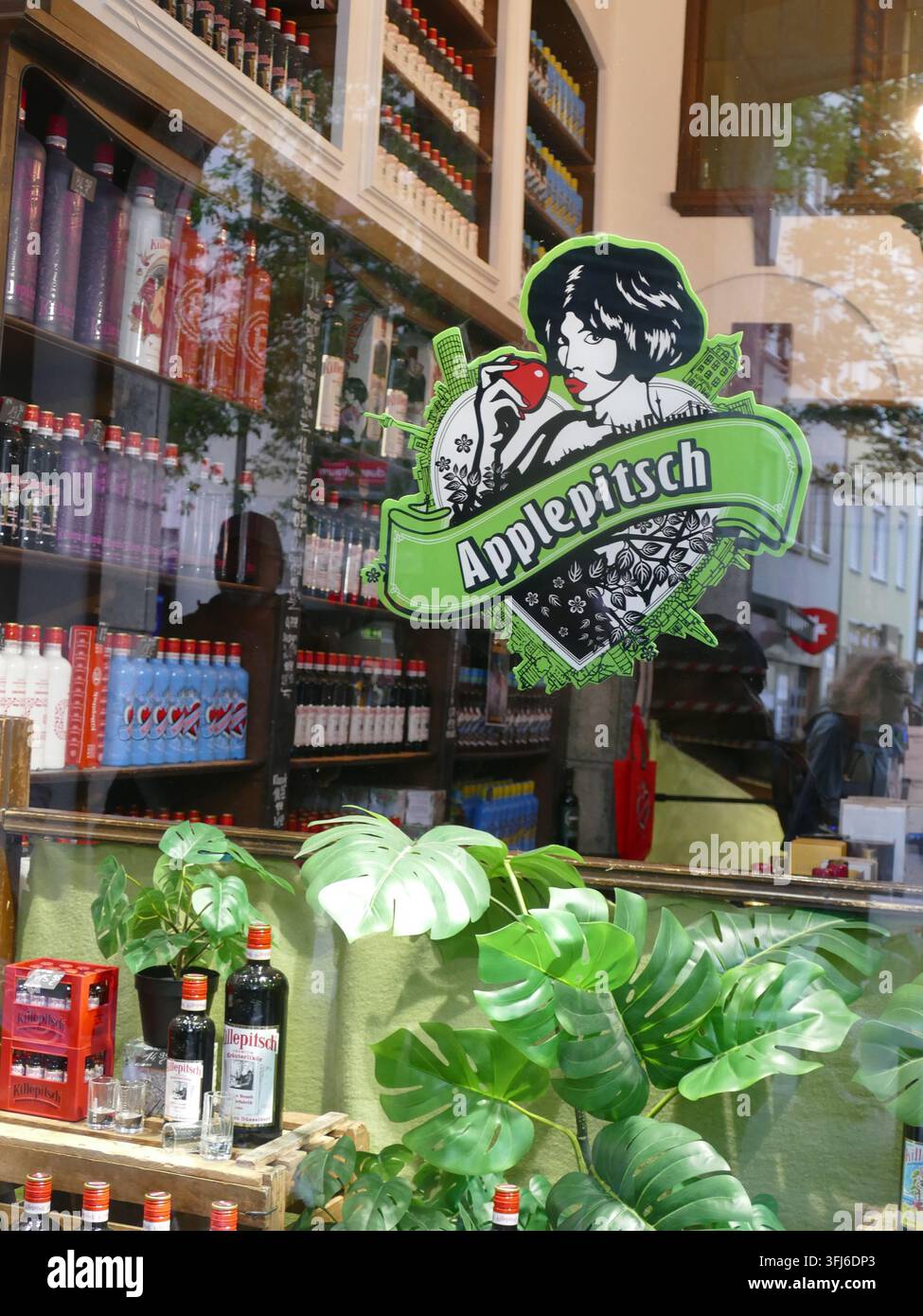 DÜSSELDORF, GERMANIA - 24 MAGGIO 2025 - Vetrina in vetro con bottiglie di schnaps alle mele, sfondo con vetrina vintage con elementi botanici e branding Foto Stock