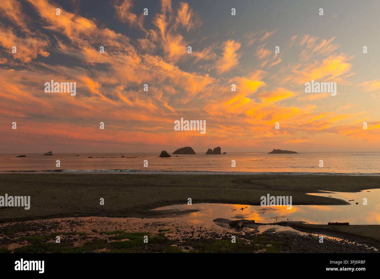 Tramonto, nuvole cumulus che sovrastano la costa nord del Pacifico, bassa marea, torrente interno che sfocia nella baia, isole rocciose, California. Foto Stock