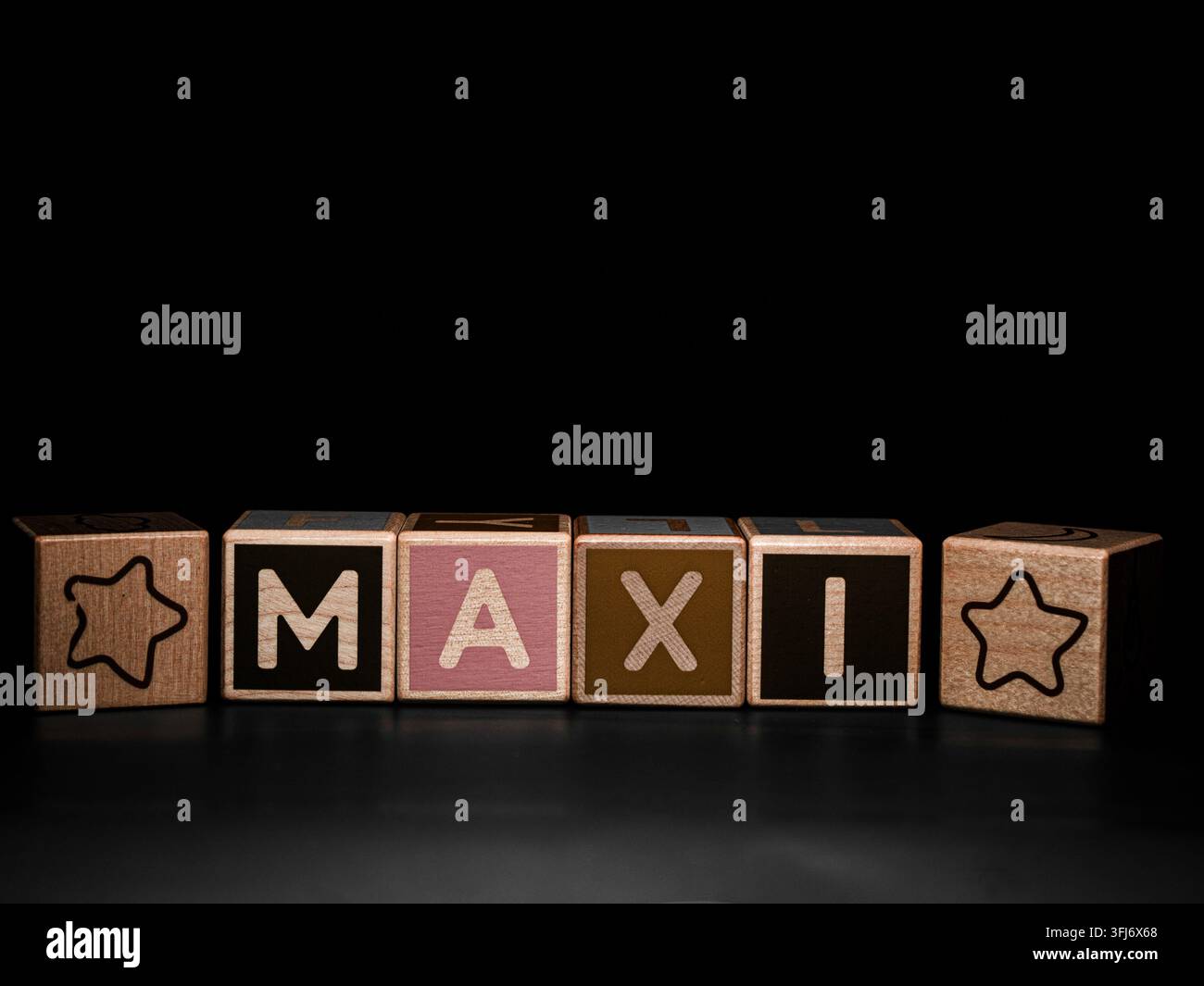 Blocchi alfabetici di legno che compongono MAXI con simboli di stelle, disposti su uno sfondo nero con ampio spazio per il testo sopra. Foto Stock