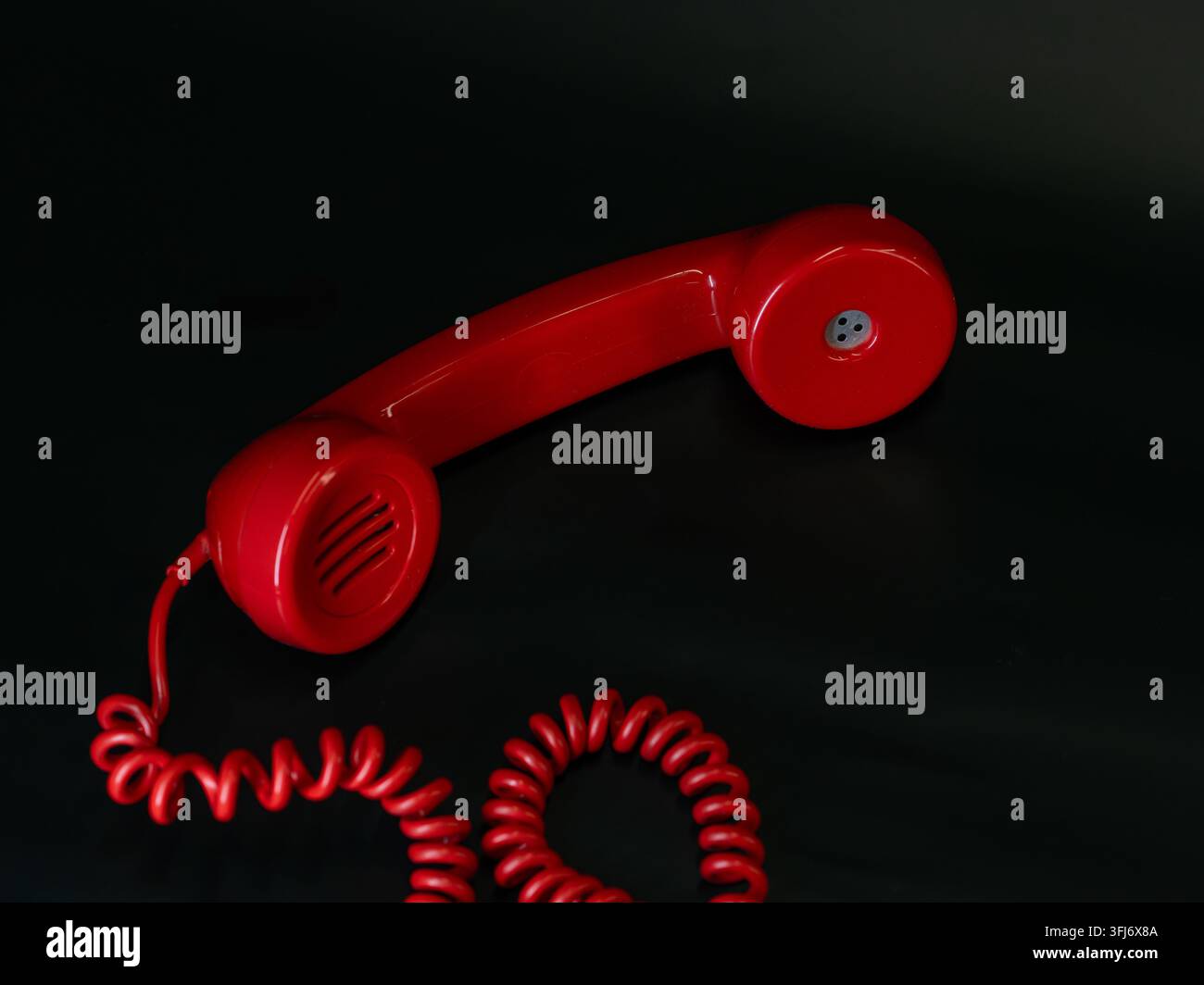 Ricetrasmittente telefonico vintage rosso con cavo a spirale isolato su uno sfondo nero scuro. Foto Stock