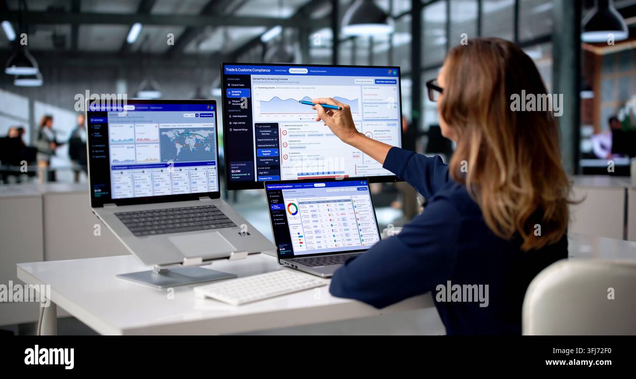 Ufficiale di conformità doganale che esamina attentamente documenti di commercio internazionale su un laptop. Foto Stock