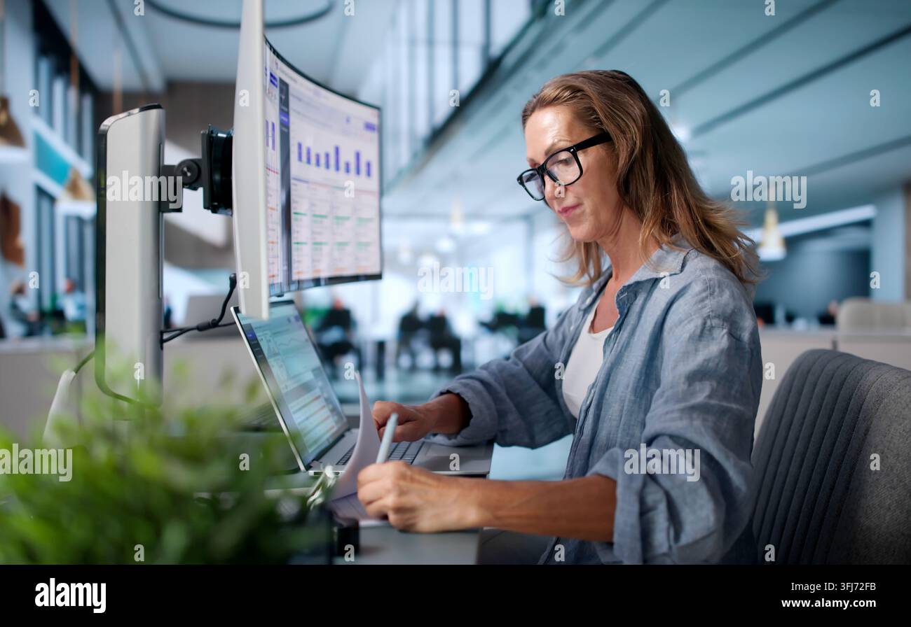 Il responsabile contabile esamina con attenzione le crediti in ritardo su un monitor ultrabreedo curvo, tracciando pagamenti e controversie Foto Stock