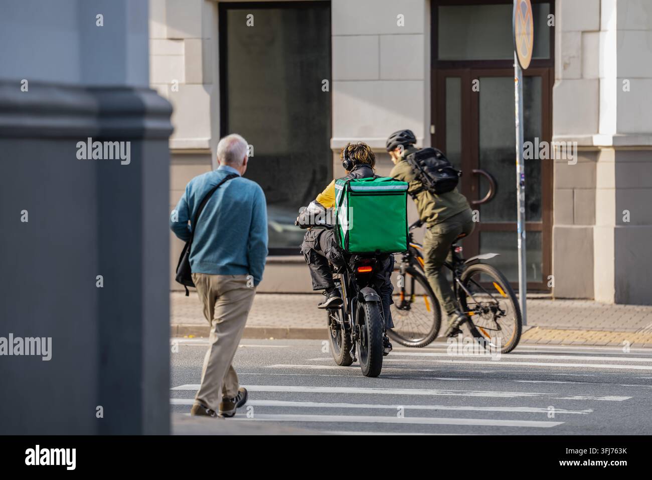 Corriere di consegna con uno zaino termico su un passaggio pedonale accanto a un ciclista, che illustra il trasporto urbano di corriere alimentare e l'ultima miglia d Foto Stock
