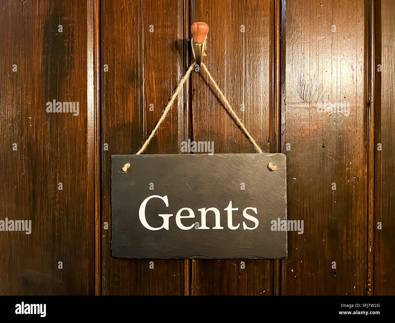 Una corda per porta in ardesia appesa tramite una corda e un gancio sul retro della porta del bagno degli uomini Foto Stock