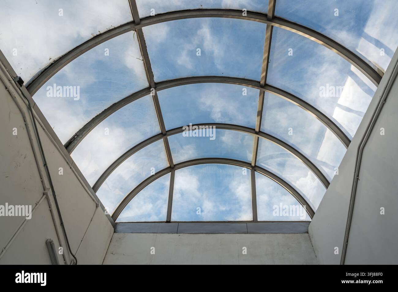 Vista ad angolo basso di un lucernario in vetro curvo con cielo azzurro e nuvole bianche Foto Stock