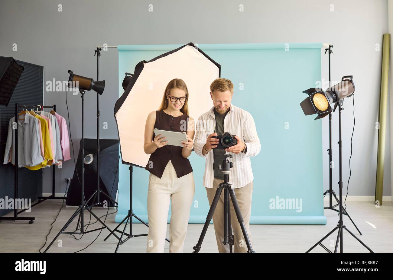 Fotografo e assistente esaminano la fotocamera in studio con attrezzatura per l'illuminazione e sfondo Foto Stock