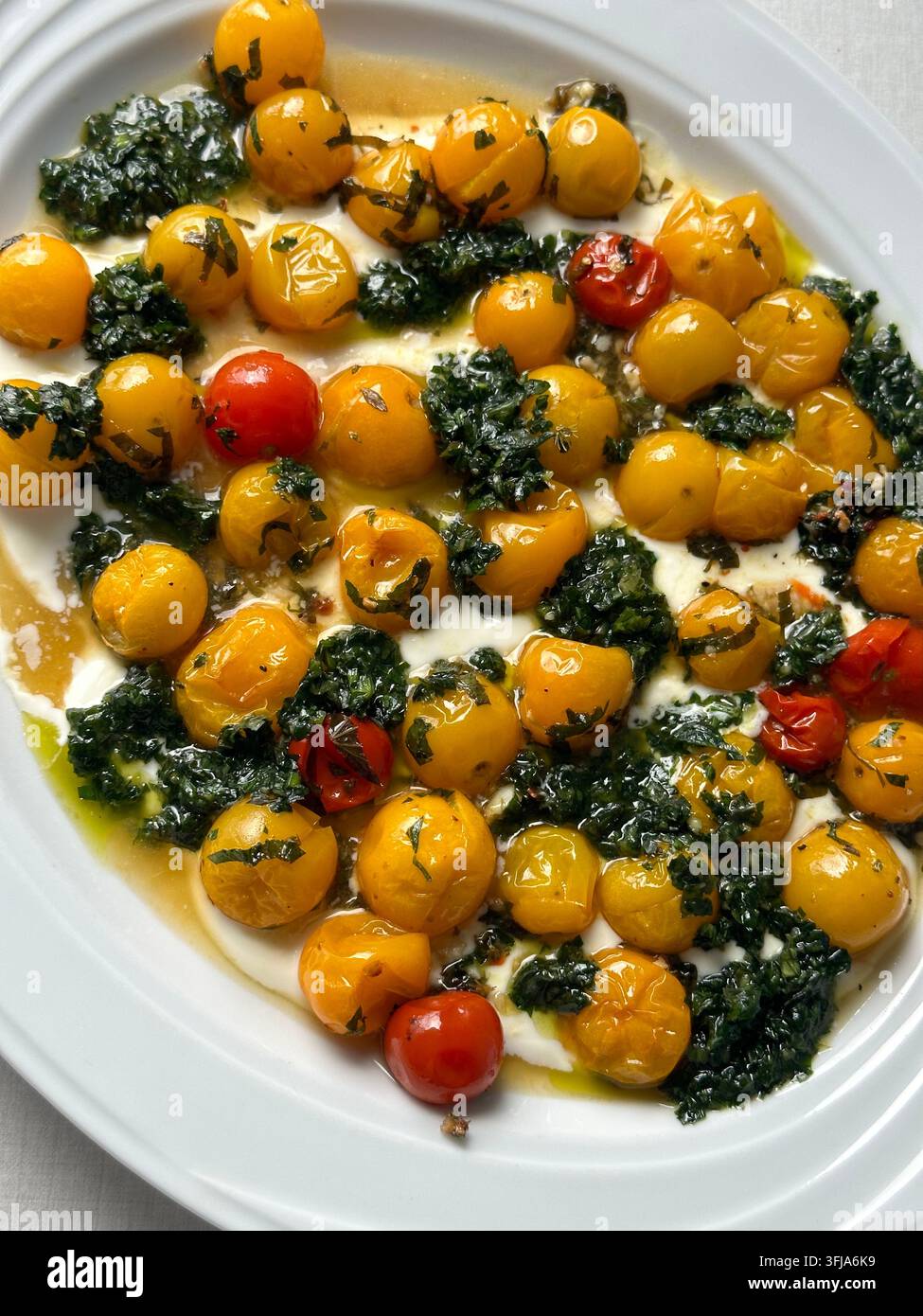 Pomodorini rossi arrostiti con pesto alle erbe verdi e formaggio cremoso su un piatto bianco. Pomodorini gialli e rossi arrostiti con olio d'oliva, gr - Immagine stock catturata con smartphone