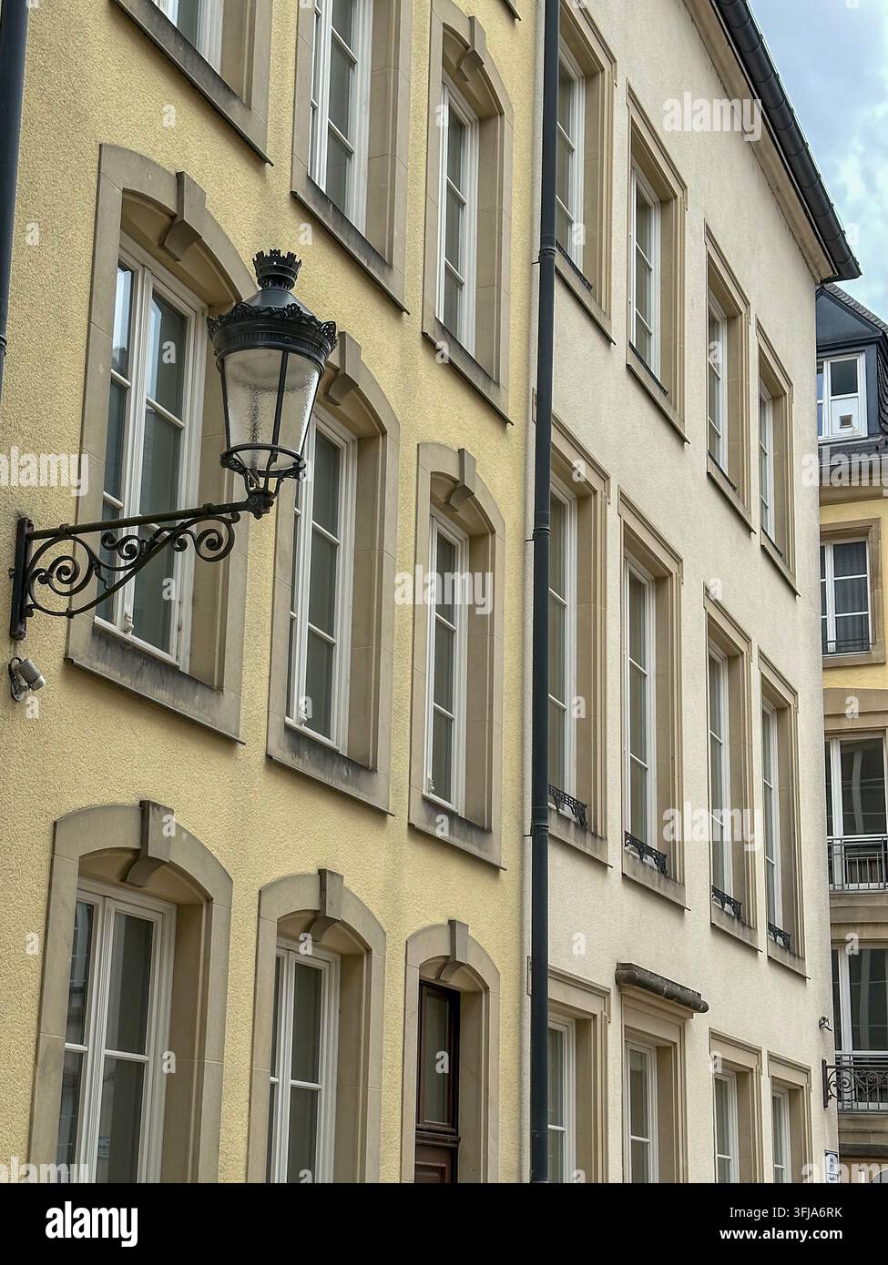 Facciata storica gialla di un edificio europeo con finestre classiche e lampione vintage. Facciata storica gialla di un edificio con file di archi classici - Immagine stock catturata con smartphone