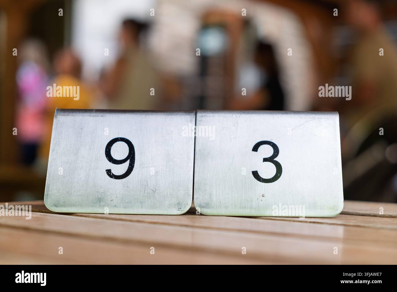 Due cartelli di metallo con i numeri 9 e 3 su una superficie di legno. Nel sfondo sono visibili persone sfocate. Foto Stock