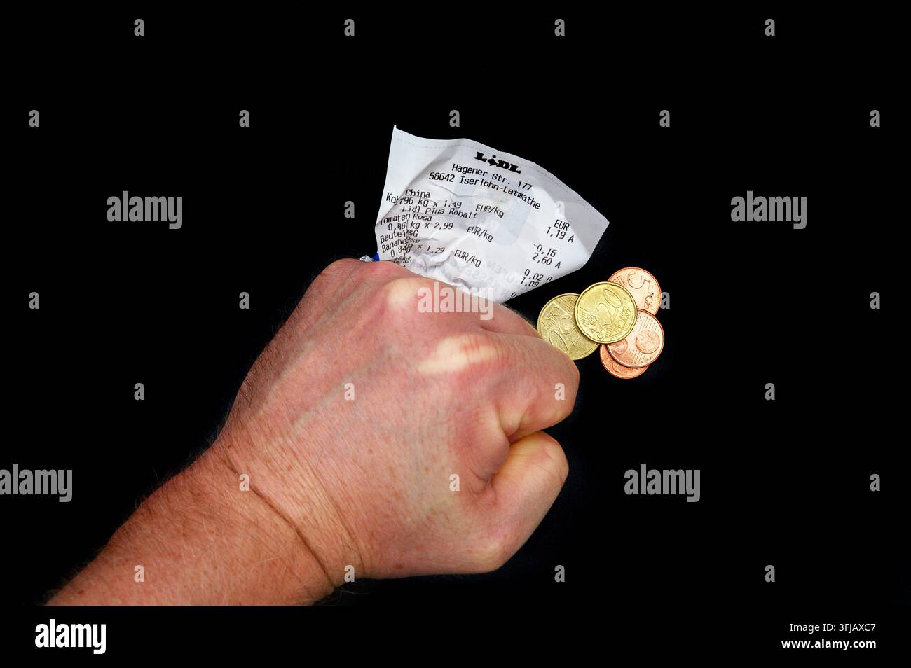 Iserlohn, Germania – 16 settembre 2026: Un pugno stretto che tiene uno scontrino della spesa Lidl accartocciato accanto a monete in euro su uno sfondo nero. Foto Stock