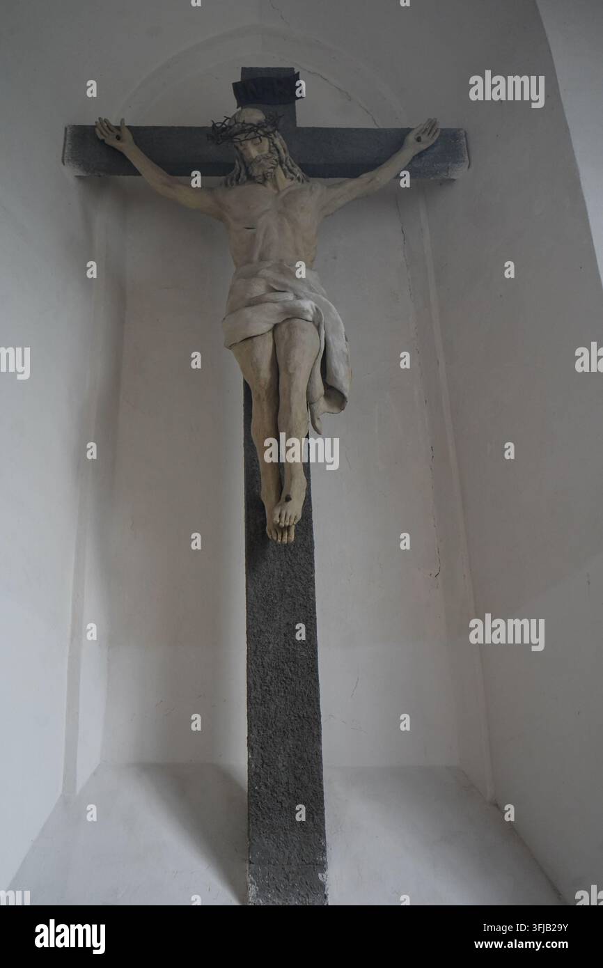 Statua classica raffigurante la crocifissione di Gesù Cristo montata su una croce scura all'interno di una tranquilla nicchia nella Chiesa Greco-Cattolica di San Bartolomeo. Foto Stock