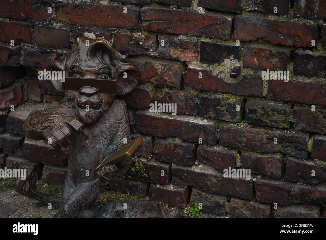 Una piccola statua di leone in bronzo di Hewelion che tiene un libro attaccato a un vecchio muro di mattoni nel centro storico della città di Danzica, Polonia. Foto Stock