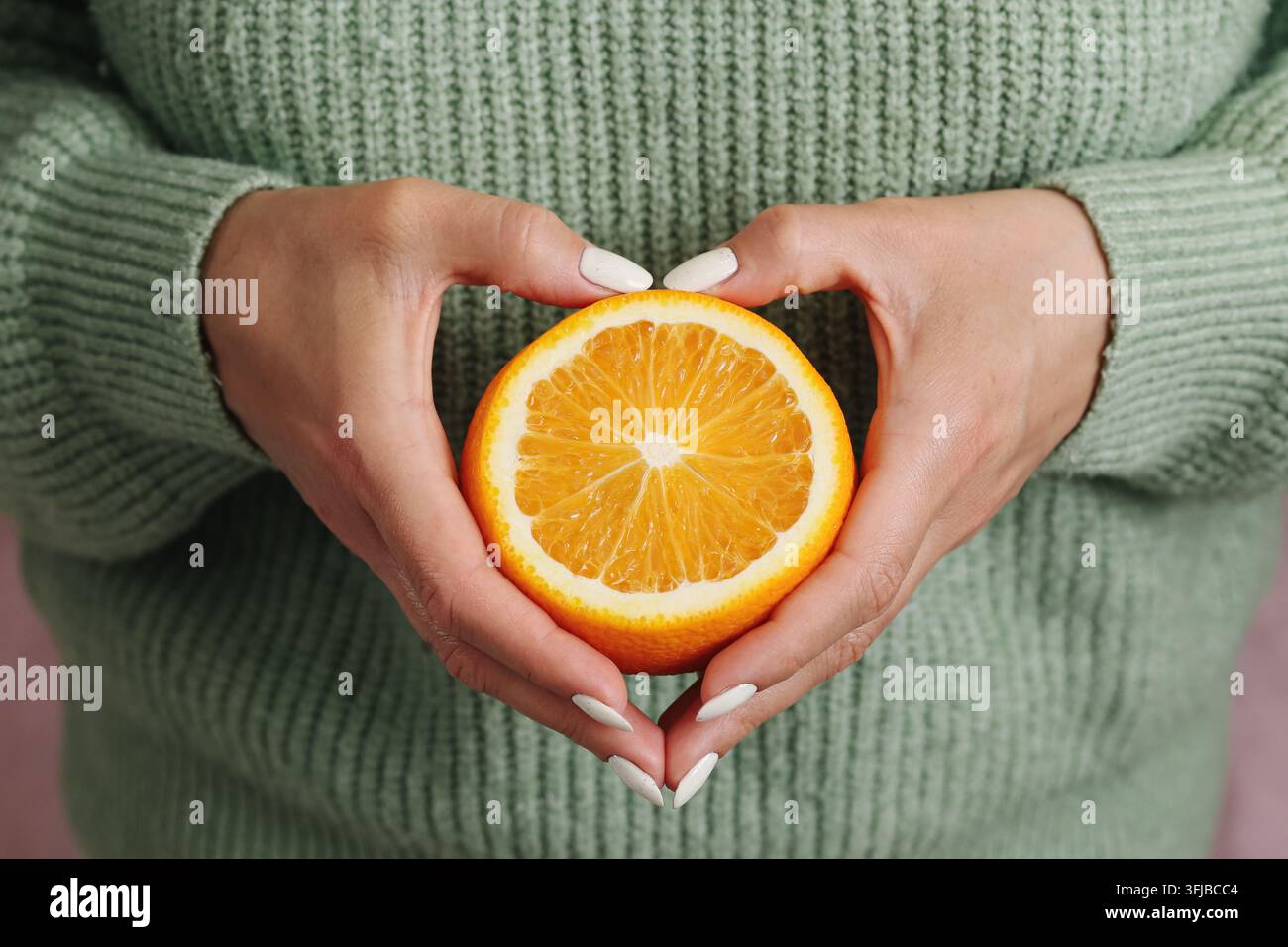 Donna che tiene una mezza arancia fresca in entrambe le mani. Sfondo di cibo sano per la nutrizione con frutti agrumi ricchi di vitamina C, benessere, freschezza e dieta equilibrata. Foto Stock
