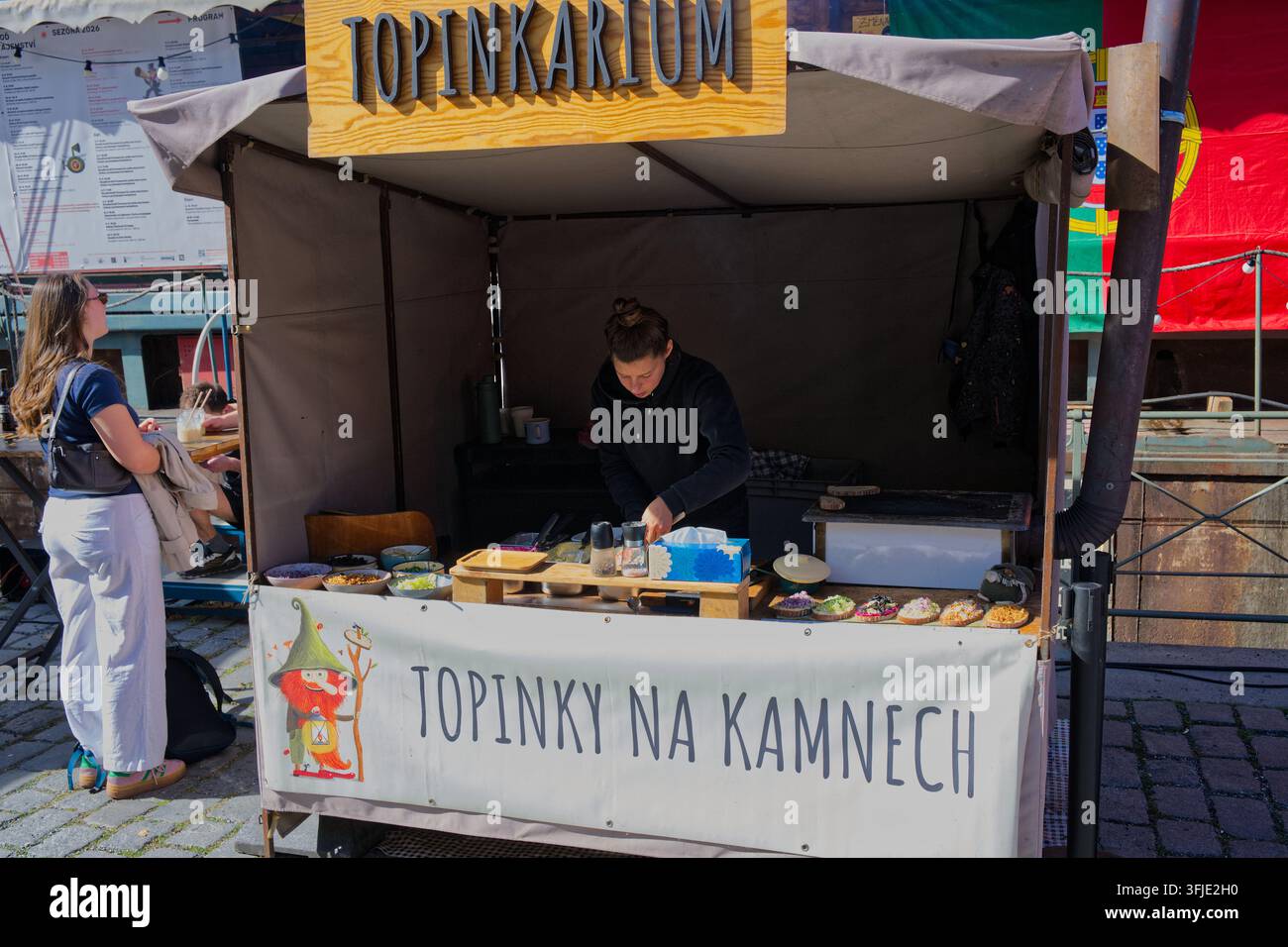 Un venditore prepara toast a faccia aperta allo stand gastronomico Topinkarium durante il mercato degli agricoltori Náplavka. Foto Stock