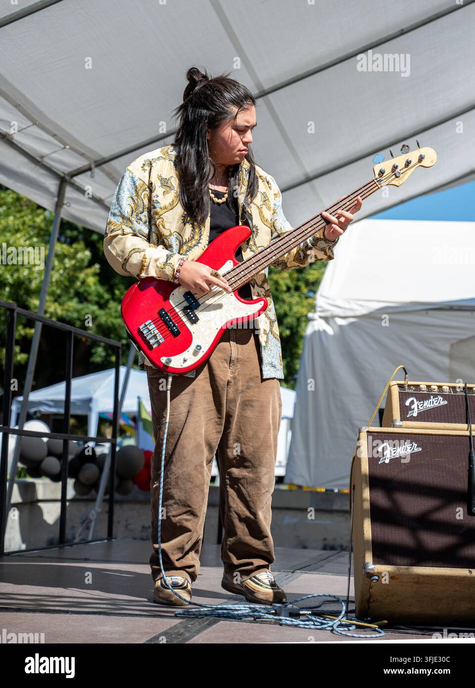 Un bassista della band Hush Hunny si esibisce sul palco durante lo Stockton Pride, suonando un basso elettrico rosso. Foto Stock