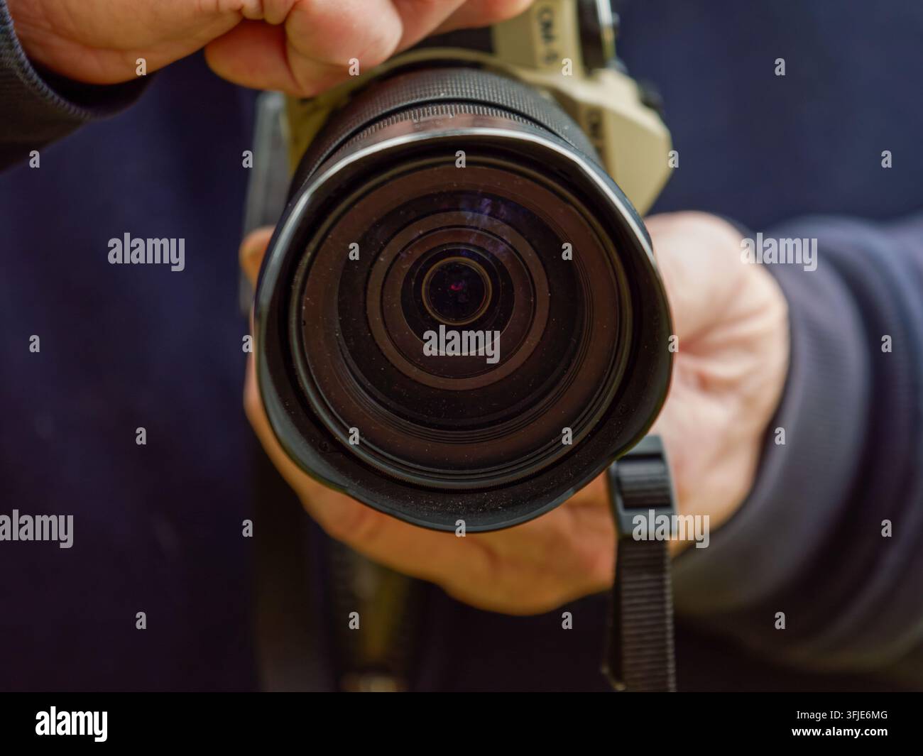 Prima piano di una persona che tiene una fotocamera con un grande obiettivo, focalizzata sull'elemento anteriore dell'obiettivo. Foto Stock