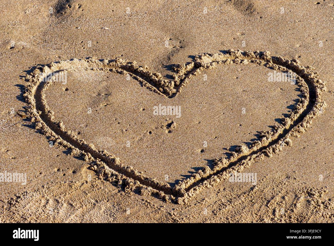 Disegno a forma di cuore nella sabbia della spiaggia che simboleggia l'amore e il romanticismo Foto Stock