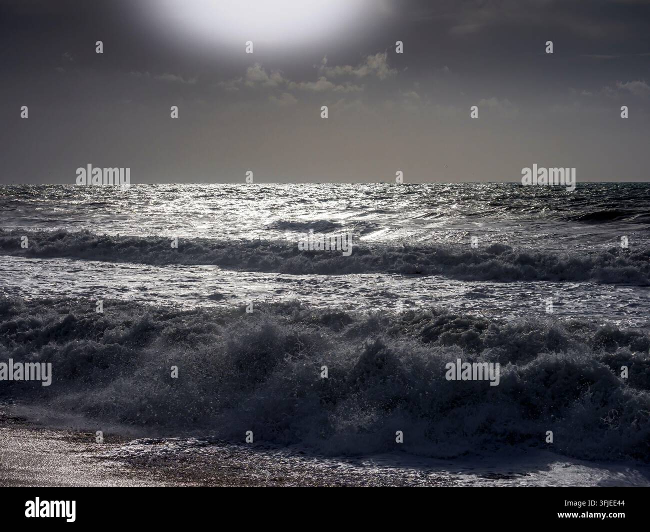 Onde del mare che si infrangono verso la riva sotto un cielo nuvoloso creando schiuma Foto Stock
