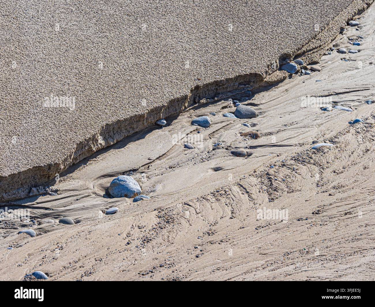 Sabbia della spiaggia che mostra modelli di erosione dovuti al flusso dell'acqua con ciottoli sparsi Foto Stock
