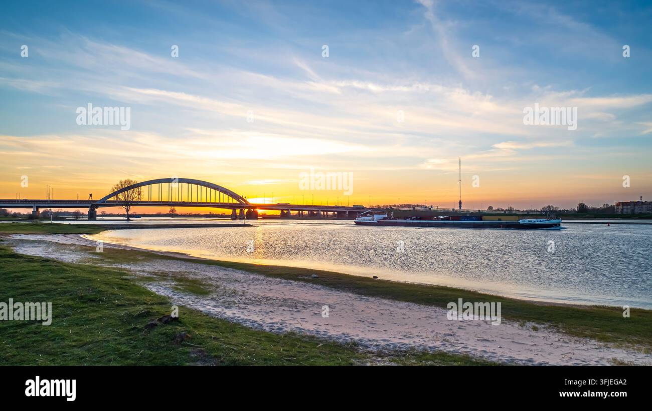Chimera che naviga lungo il fiume Lek oltre il ponte Lek di Vianen durante l'ora dorata, riflettendo colori vivaci del tramonto sull'acqua, in contrasto con il ponte Jan Blanken - Questa è un'immagine storica che mostra il ponte Lek, rimosso nel 2021 Foto Stock