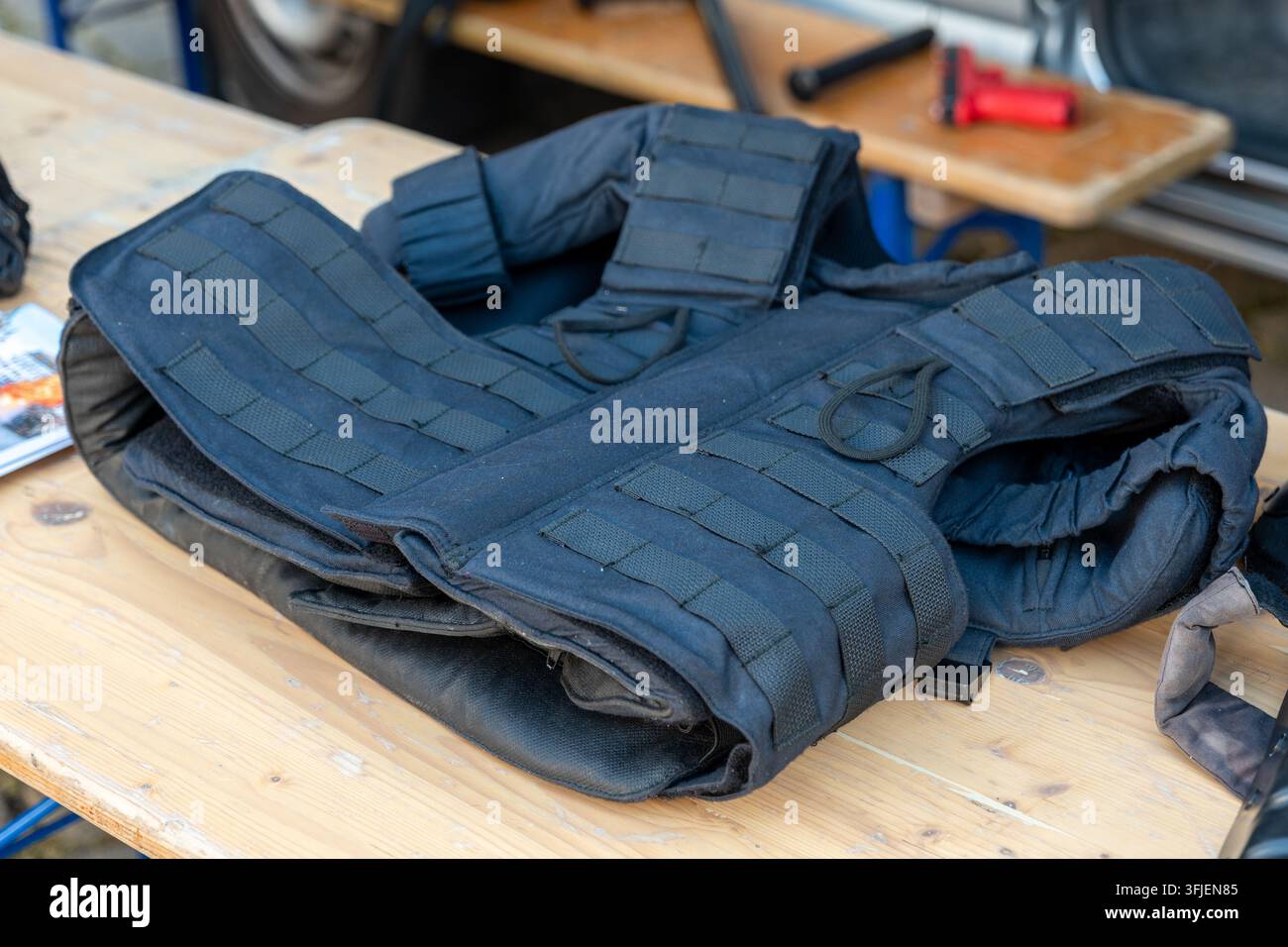 Un giubbotto antiproiettile tattico giace piegato su un banco di lavoro in legno in un'officina. Foto Stock