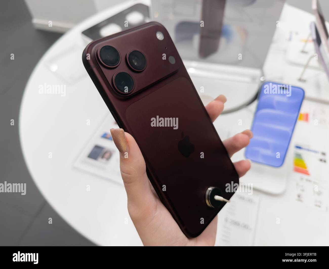 Pozna, Polonia – 19 settembre 2026: Smartphone Apple iPhone 18 Pro bordeaux mostrato da un acquirente durante una visita al negozio al dettaglio per esibire un'estetica elegante Foto Stock