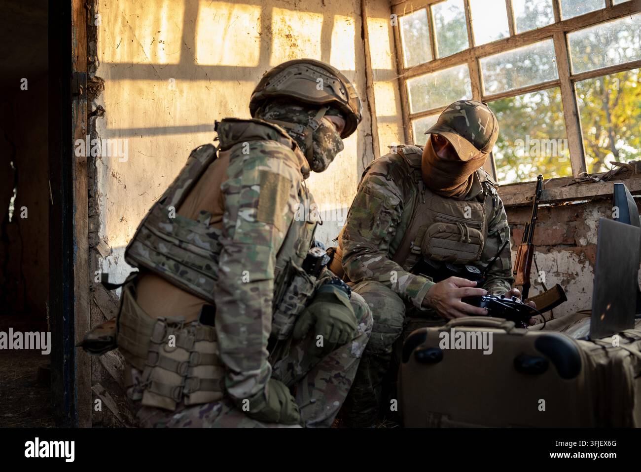 I soldati gestiscono una console di controllo dei droni. Il personale militare sta svolgendo una missione di combattimento in una posizione in una vecchia casa abbandonata. Foto Stock