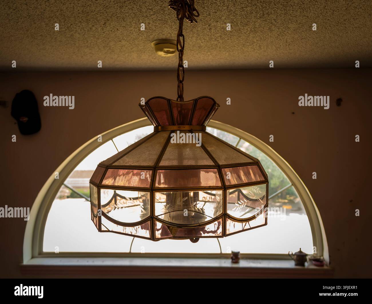 Lampada a sospensione vintage in vetro colorato appesa davanti a una finestra semicircolare all'interno di un ambiente retrò Foto Stock