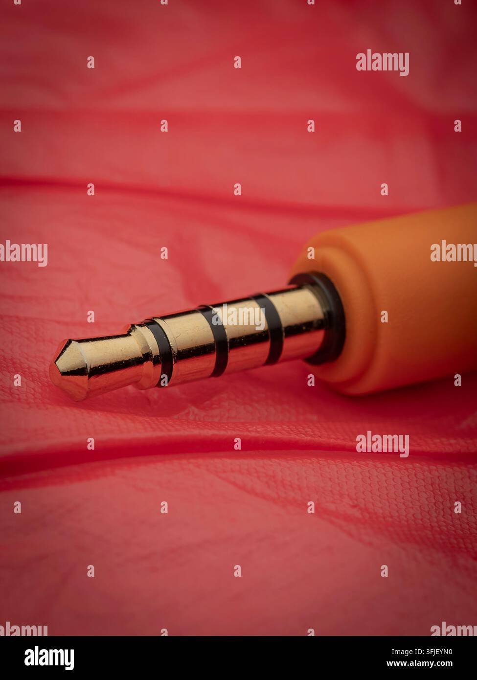 Macro close-up di un connettore jack audio dorato con involucro arancione su una superficie di fondo rosso vivace Foto Stock