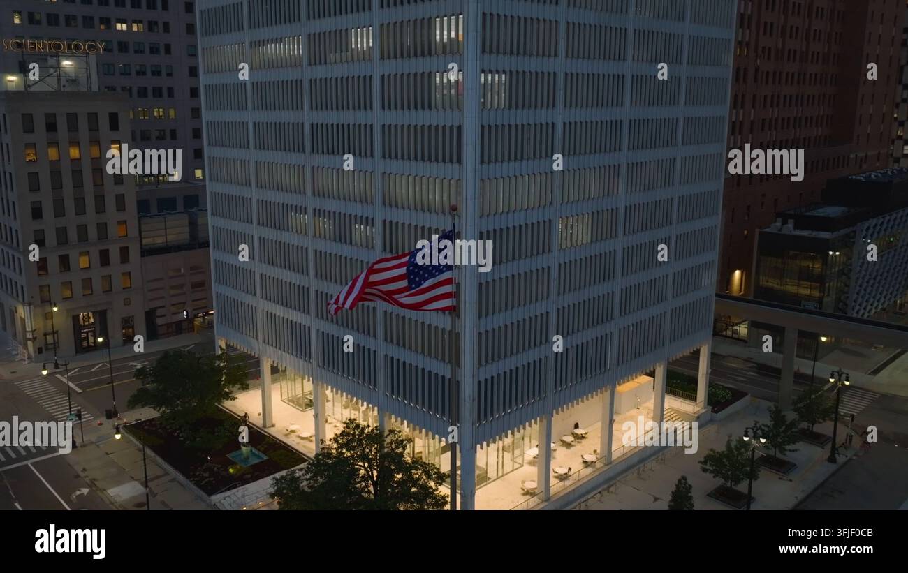 Edificio municipale del centro città in America. Bandiera americana che sventola fuori da un moderno edificio governativo. Ripresa aerea con drone di notte, Detroit, Michigan. Foto Stock
