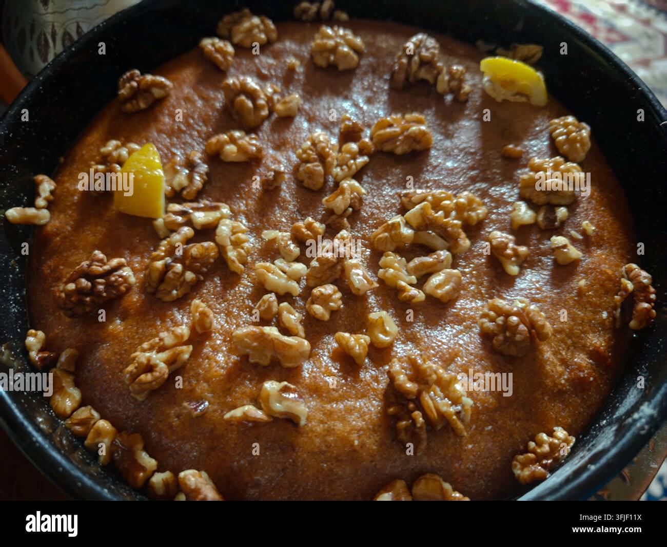 Una vista ravvicinata dall'alto di una torta di semola Mevlud appena sfornata, splendidamente decorata con noci sane e pezzi di agrumi. - Immagine stock catturata con smartphone