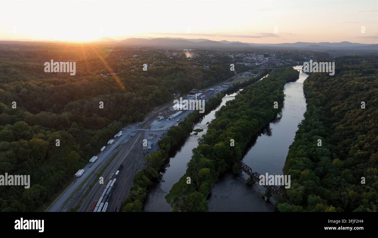 Binari ferroviari con treno merci parcheggiato vicino al fiume James e all'impianto di trattamento delle acque reflue in Virginia. Raggi del sole dell'alba dorata al mattino. Vista aerea ampia Foto Stock