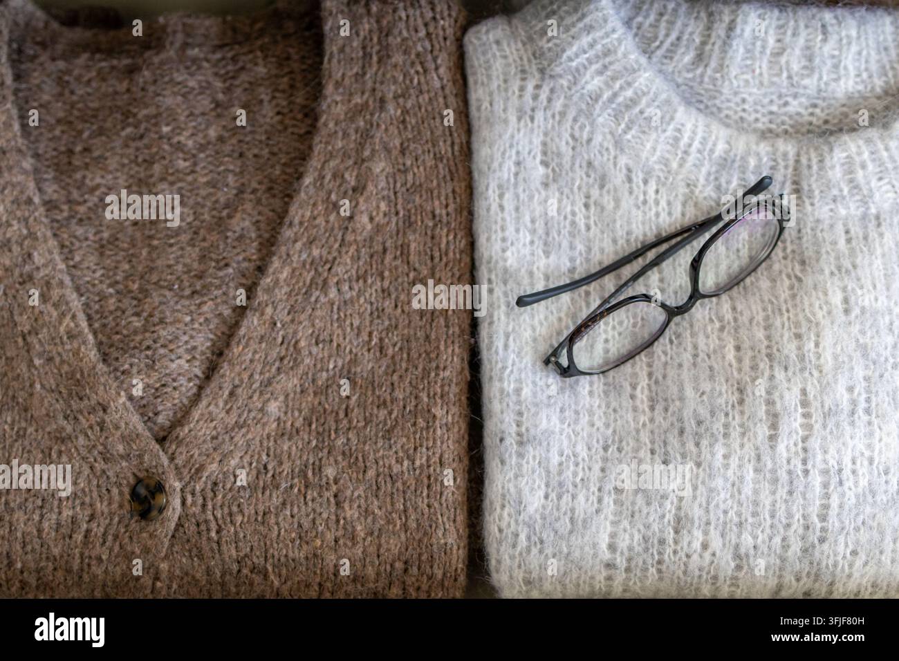 Cardigan e maglione piegati affiancati con occhiali appoggiati sul tessuto. Concetto di stile di guardaroba autunnale accogliente e presentazione di maglieria Foto Stock
