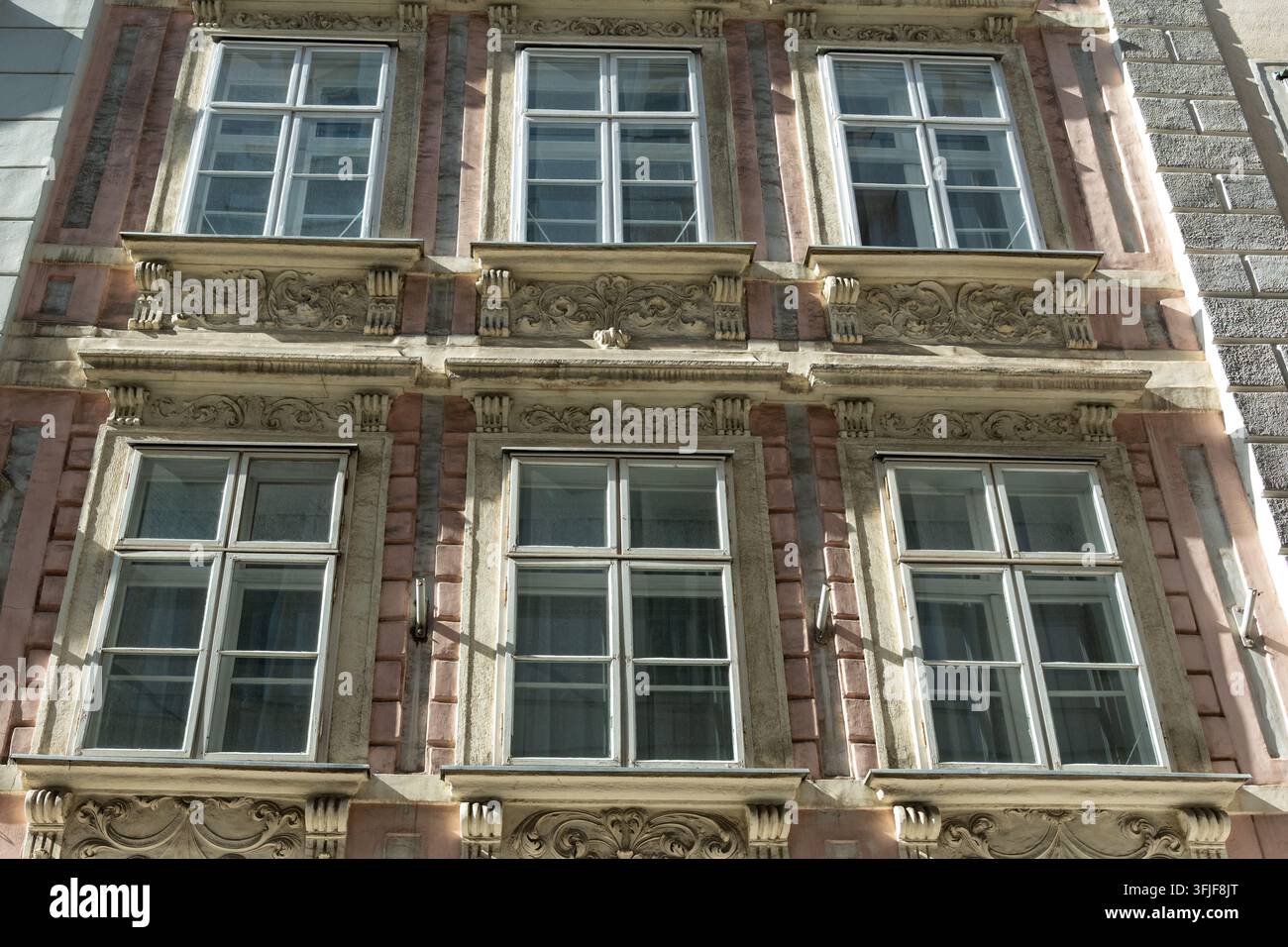 Una facciata di edificio storico ornata presenta finestre simmetriche, lavori di pietra decorativi e dettagli architettonici illuminati dal sole. Foto Stock