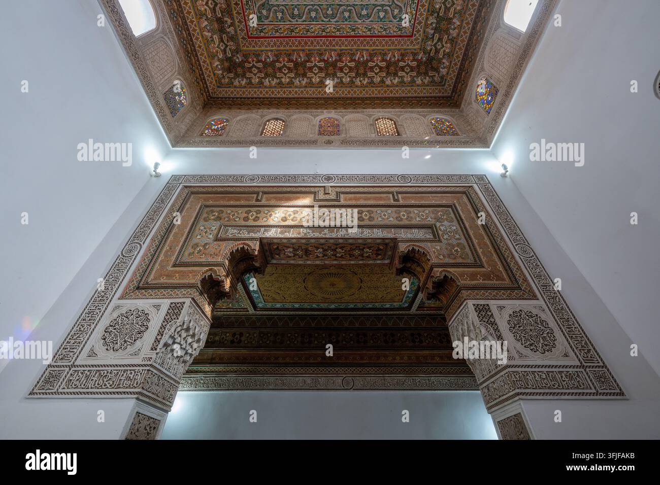 Un soffitto dipinto ornato, un arco in stucco intagliato e piastrelle geometriche decorano un passaggio interno del Palazzo Bahia a Marrakesh, Marocco. Foto Stock
