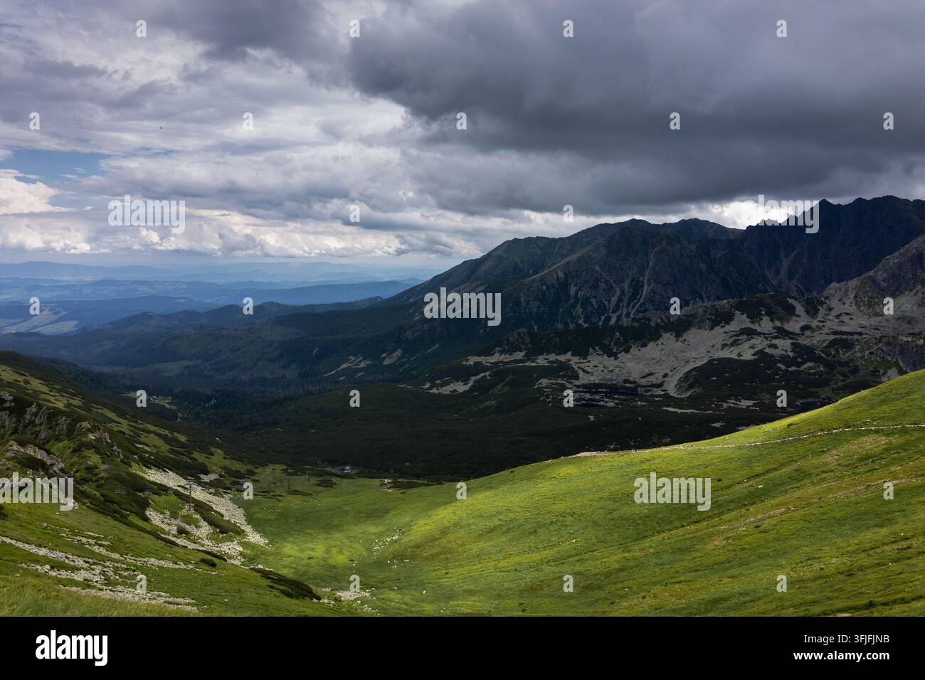 Vista drammatica della catena montuosa dell'Alta Tatracia e di un pendio erboso verde sotto nuvole tempestose scure Foto Stock