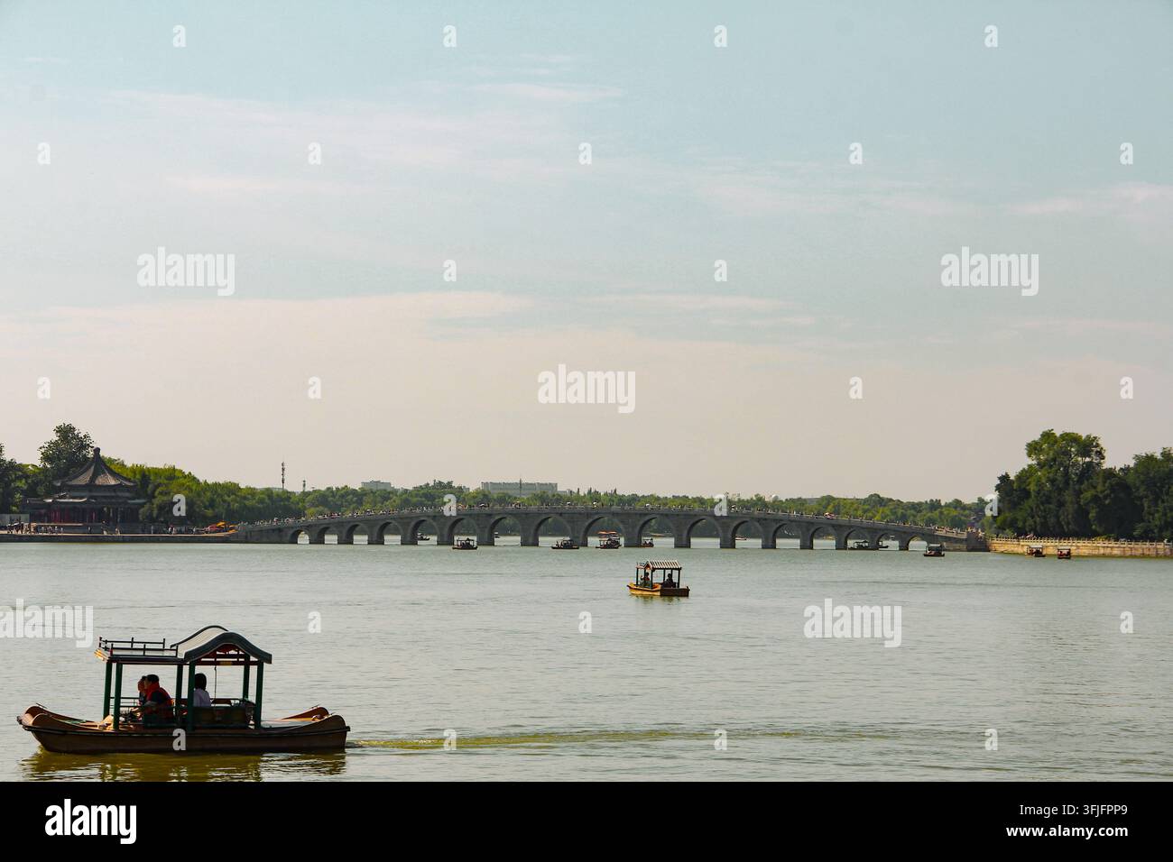 Barche di legno tradizionali sul lago Kunming con il ponte dei diciassette archi storico e l'architettura imperiale del palazzo d'estate a Pechino, in Cina. Foto Stock