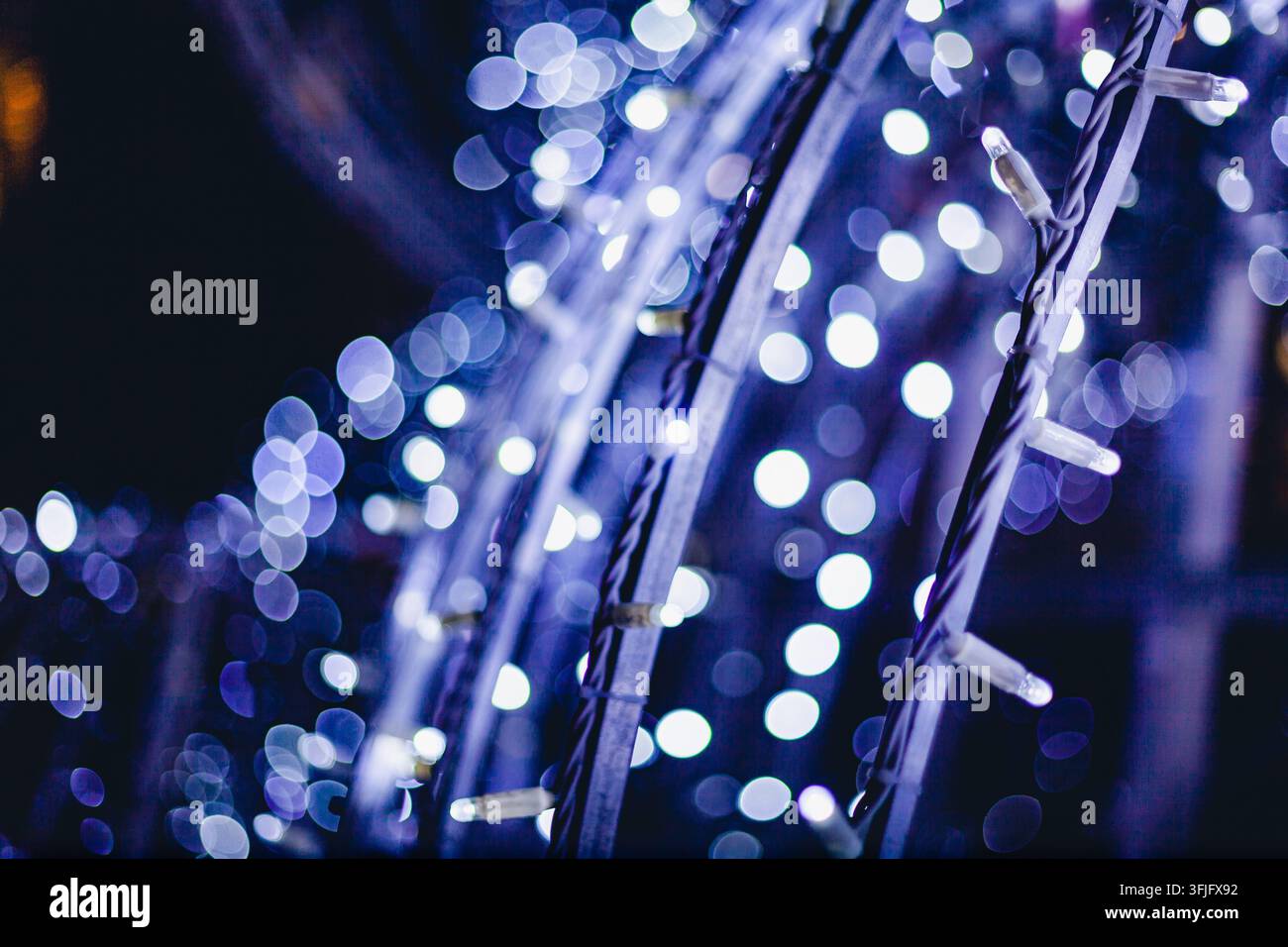 Prima vista di luci a filo bianco brillante avvolte intorno ad archi strutturati che creano un effetto bokeh magico di notte. Foto Stock
