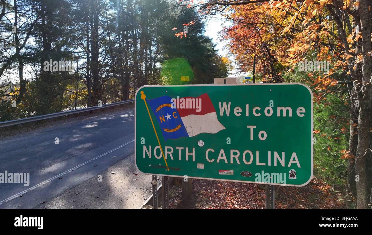 Insegna di benvenuto in Carolina del Nord lungo una strada tortuosa fiancheggiata da alberi colorati in autunno. Ripresa aerea ascendente, Contea di Surry. Foto Stock