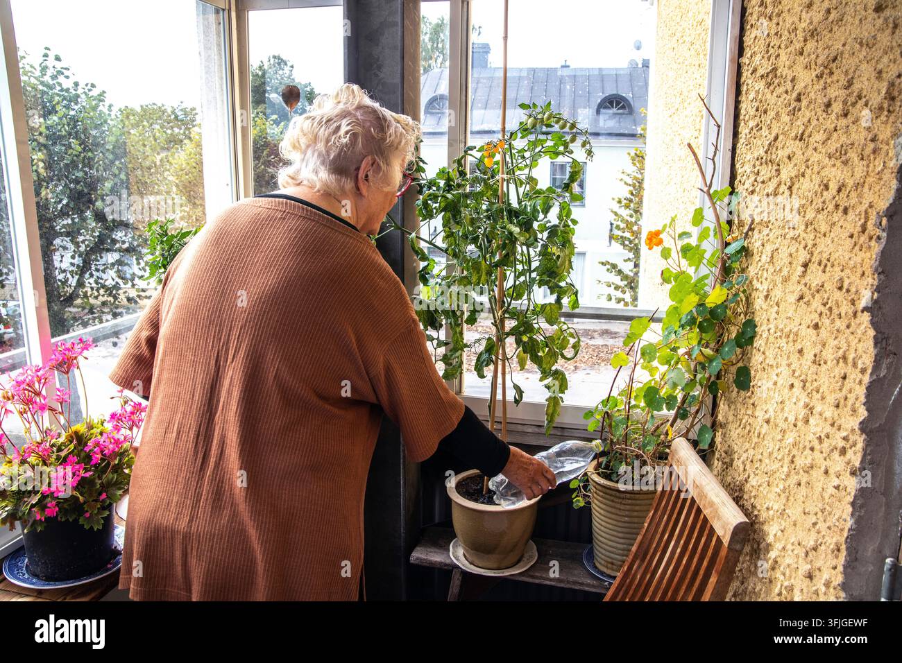 Una donna anziana sta annaffiando le sue piante sul balcone. Foto Stock