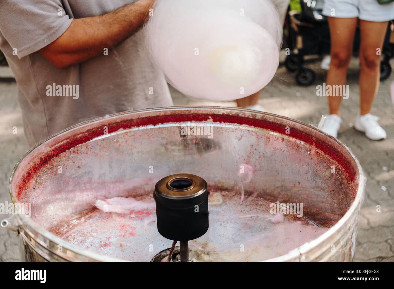 Un venditore prepara una barba di zucchero rosa con una macchina rotante per lo zucchero all'aperto. Scena di cibo divertente per fiere, festival, intrattenimento familiare e pasticceria p Foto Stock
