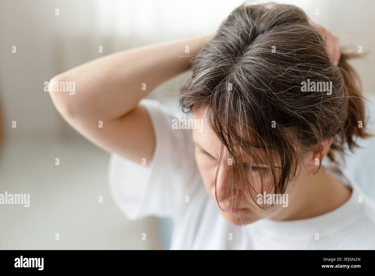 Una donna si prende delicatamente cura dei suoi capelli argentati che ingrigiscono con prodotti speciali ogni giorno. L'adulta matura impara la routine migliore per mantenere la salute delle ciocche. La madre dedica tempo alle esigenze dei suoi capelli invecchianti. Foto Stock