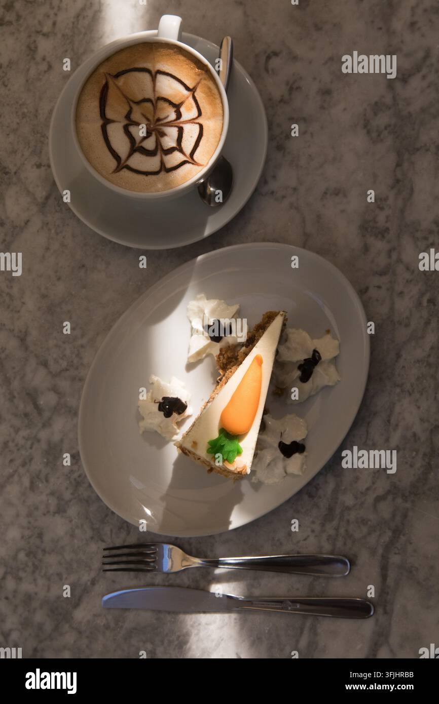 Un cliente si gode una torta di carote e un cappuccino per un dolce spuntino pomeridiano. Foto Stock