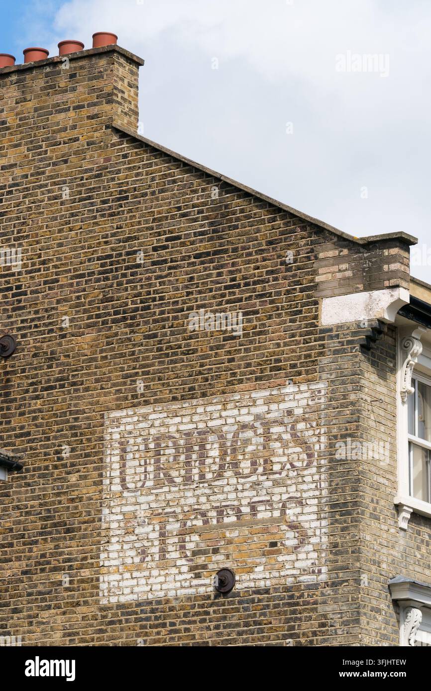 Un cartello fantasma vintage "Urquhart's" sbiadito dipinto su un edificio di mattoni di Londra, che conserva la storia commerciale dell'area. Foto Stock