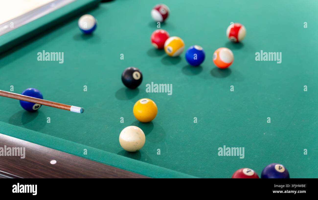 Palle da biliardo sparse su un tavolo da biliardo verde con una stecca, che mostrano una disposizione colorata pronta per una partita di biliardo. Foto Stock