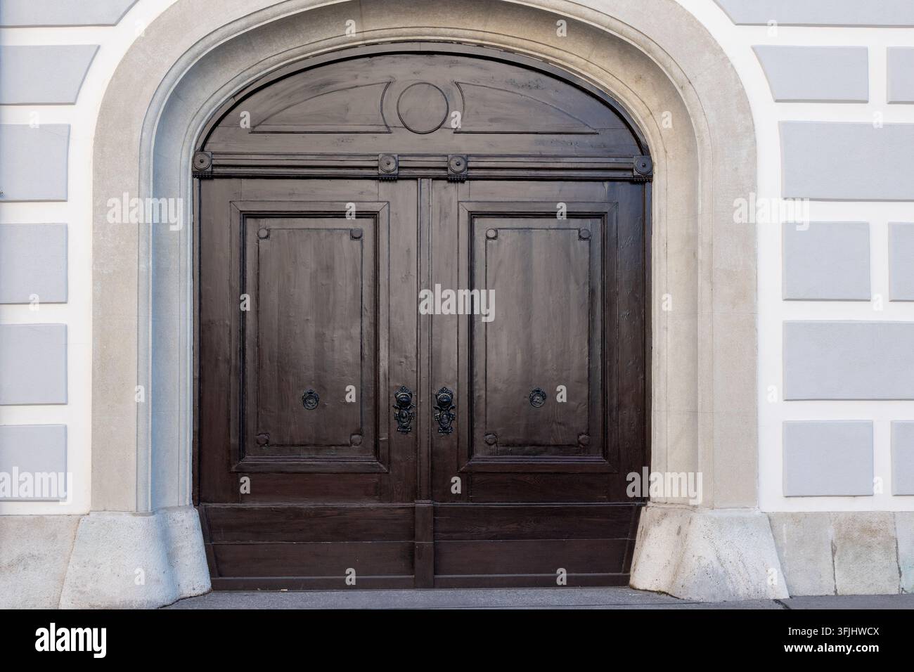 Una doppia porta in legno scuro si trova all'interno di un ingresso in pietra ad arco su una facciata chiara. Foto Stock